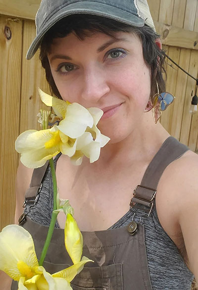 Kimberly G, horticulture student, wears earring she has created from pressed flowers and sniffs a flower