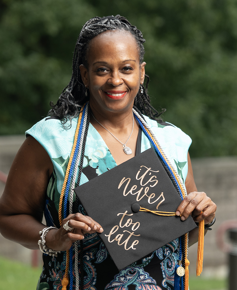 Jacqueline DeCambre holds her graduation cap which reads, "It's Never Too Late"