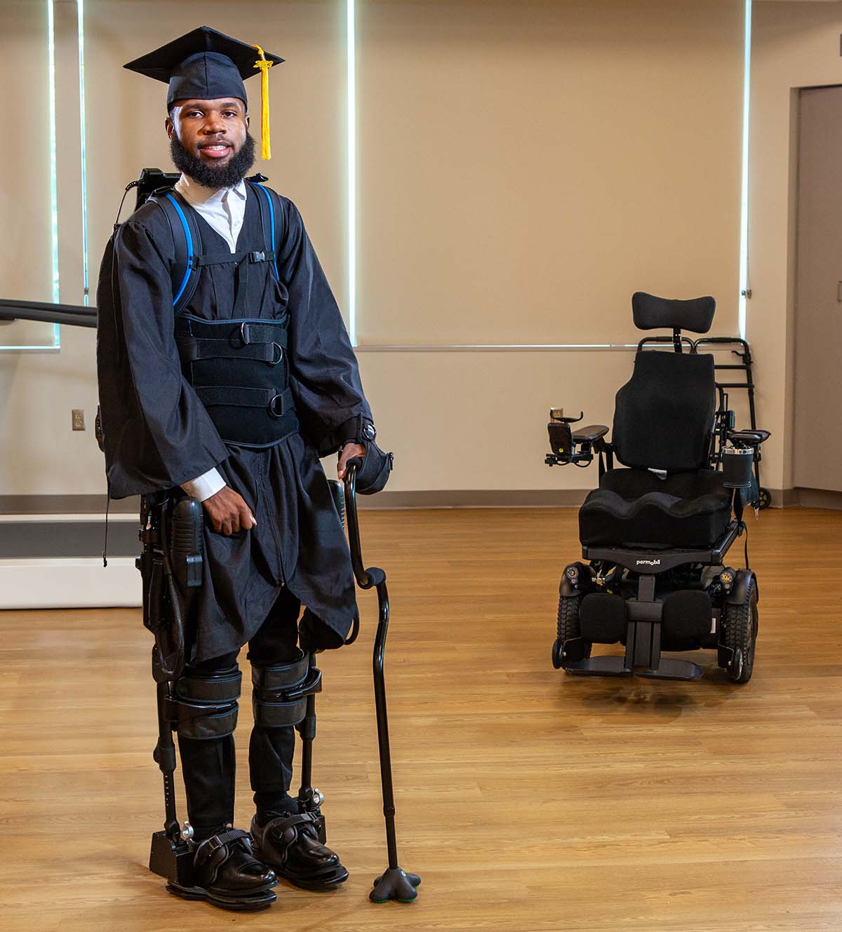 Khalil Watson wearing his graduation cap and gown, stands with the help of exoskeleton