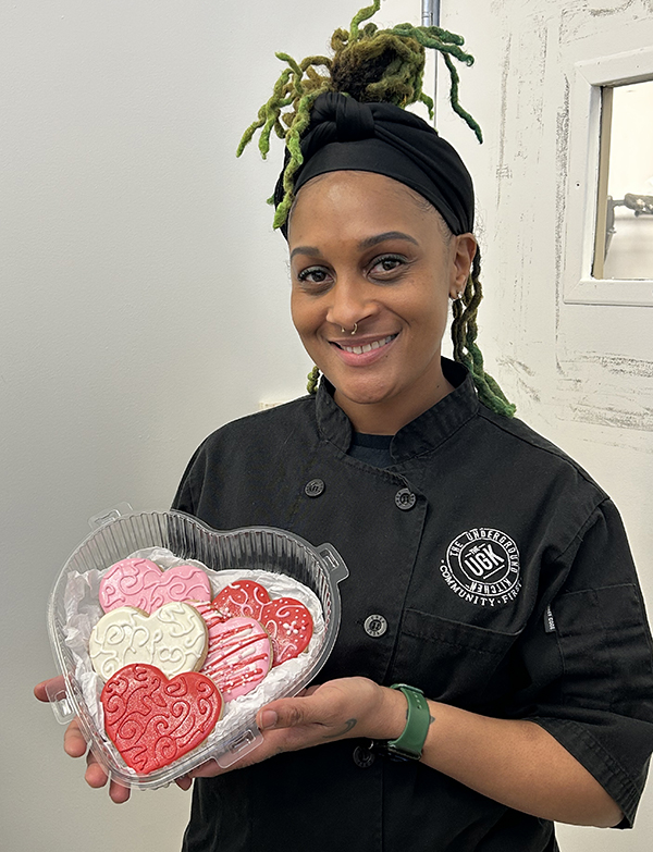 Shaye Bowser, pastry chef, dressed in black chef uniform, shows off her heart-shaped cookies