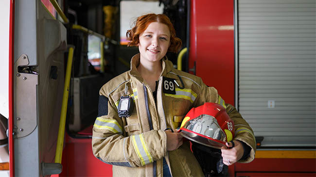 Two firefighters in uniform standing next to a red fire truck, ready to respond to an emergency.