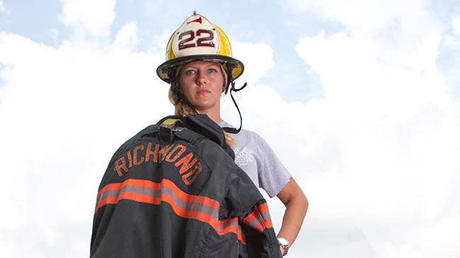 A female firefighter in uniform standing proudly in front of a red fire truck.