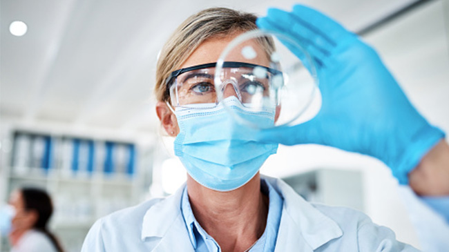 Scientist wearing lab coat and gloves analyzing glass object.