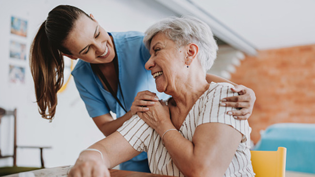 A younger woman assisting an elderly woman at a table.